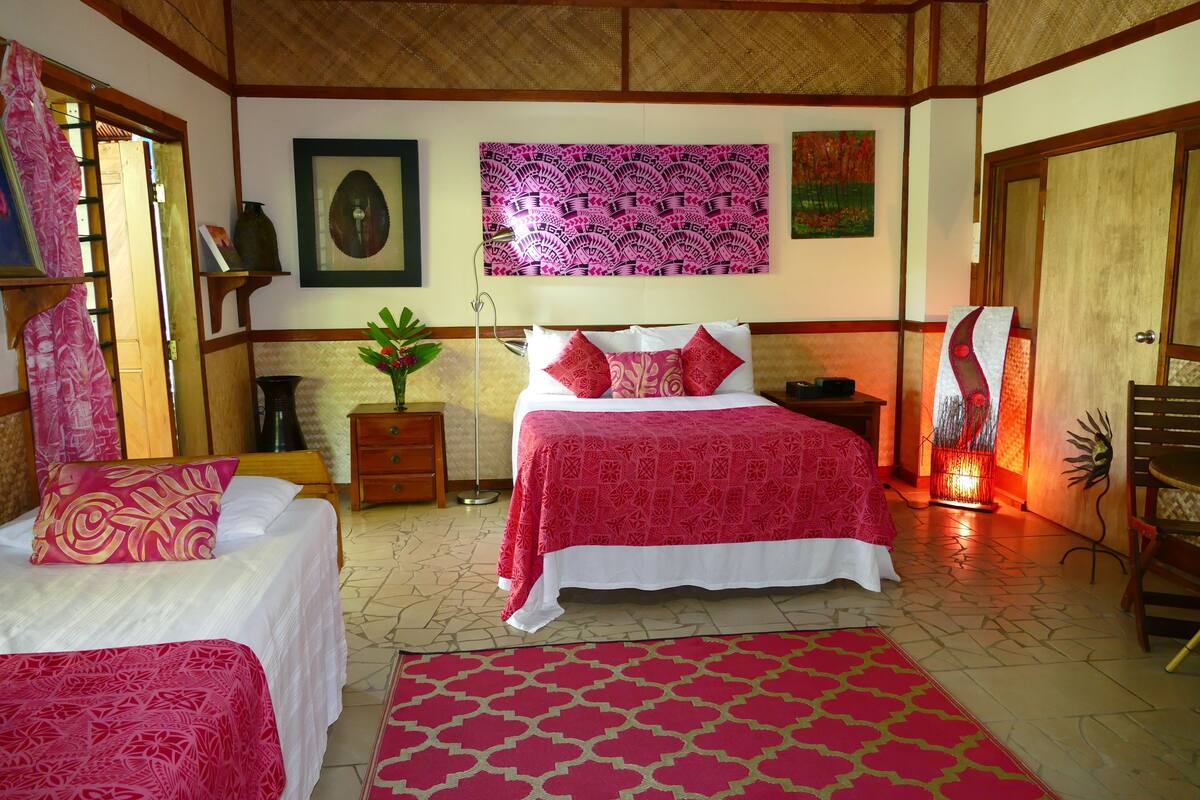 A bedroom with a bed, bedside tables, a nightstand, a lamp, a potted plant, and a painting on the wall.
