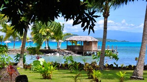 A tropical beach scene with a thatched-roof hut, palm trees, and a clear blue sea. - Le Vasa Resort (Cape Fatuosofia)