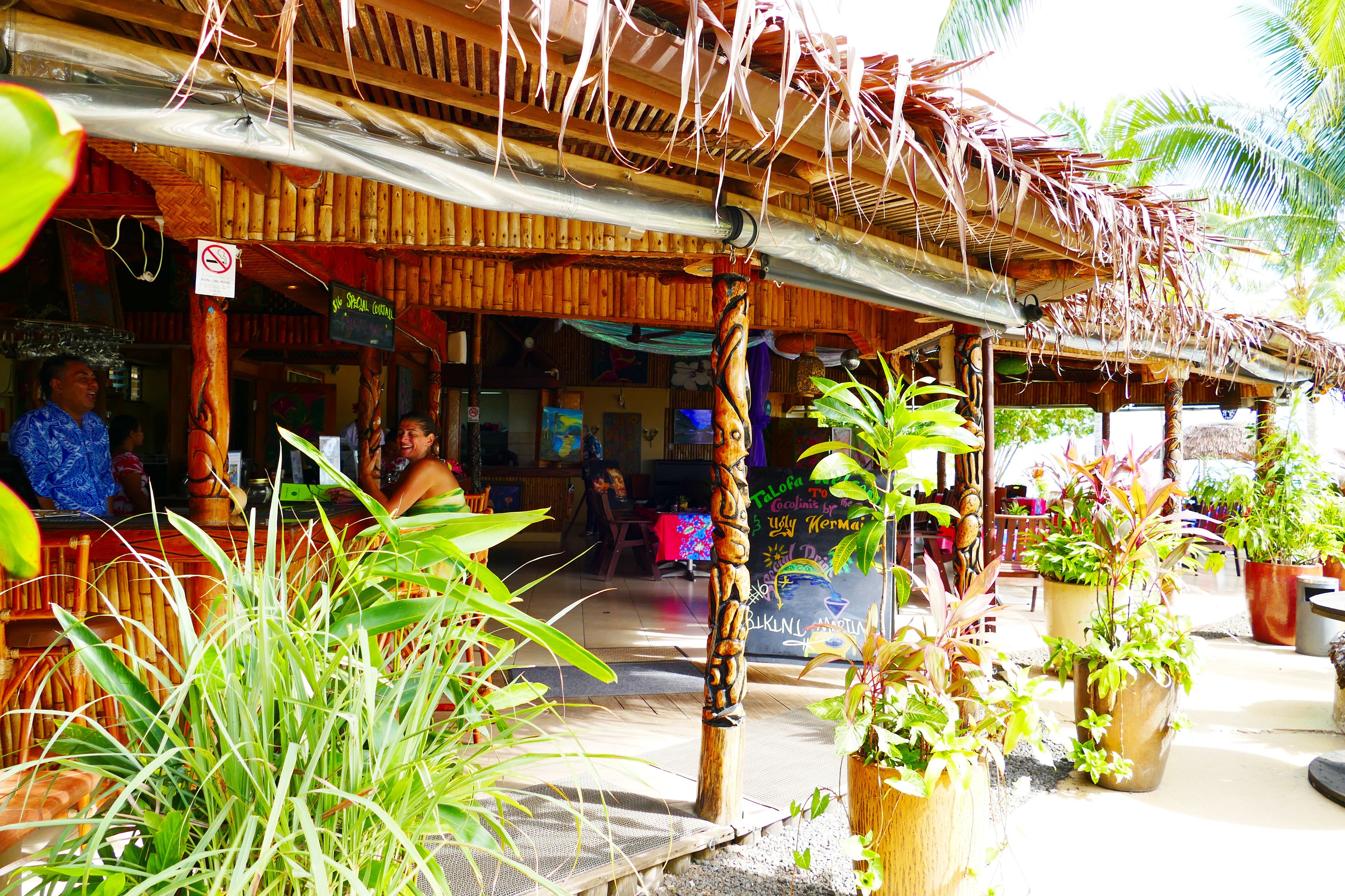 A wooden structure with a thatched roof, surrounded by potted plants and a bamboo pole.