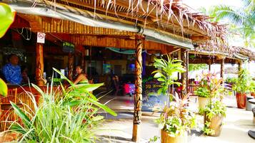 A wooden structure with a thatched roof, surrounded by potted plants and a bamboo pole.