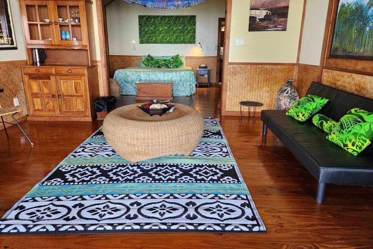 A room with a bed, a sofa, a wooden cabinet, and a woven ottoman.