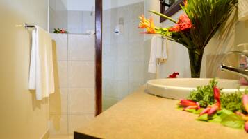 A bathroom with a shower, a sink, and a mirror. There are towels hanging on the wall and a vase with flowers on the counter.