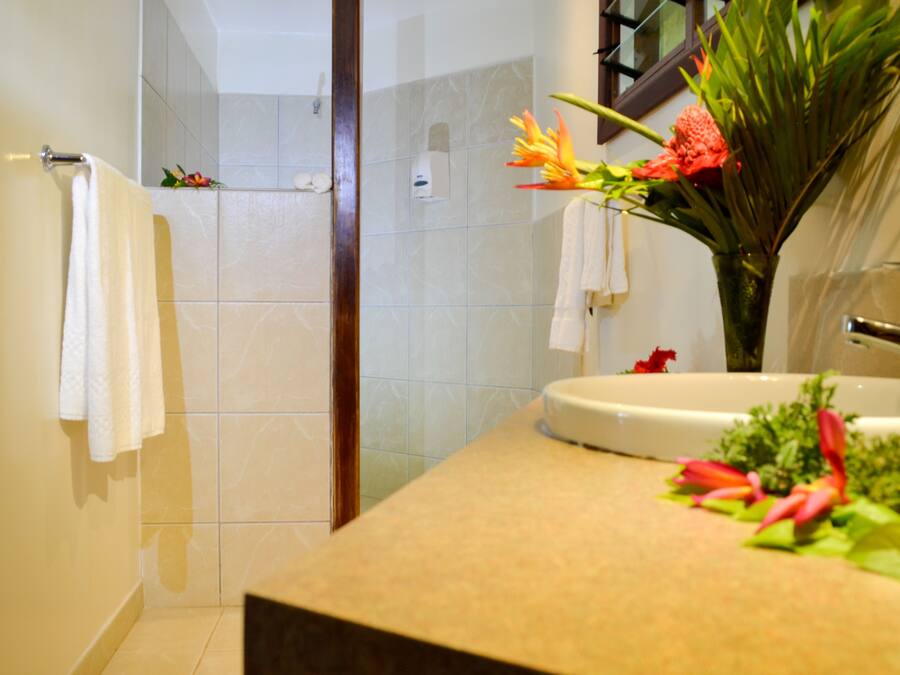 A bathroom with a shower, a sink, and a mirror. There are towels hanging on the wall and a vase with flowers on the counter.