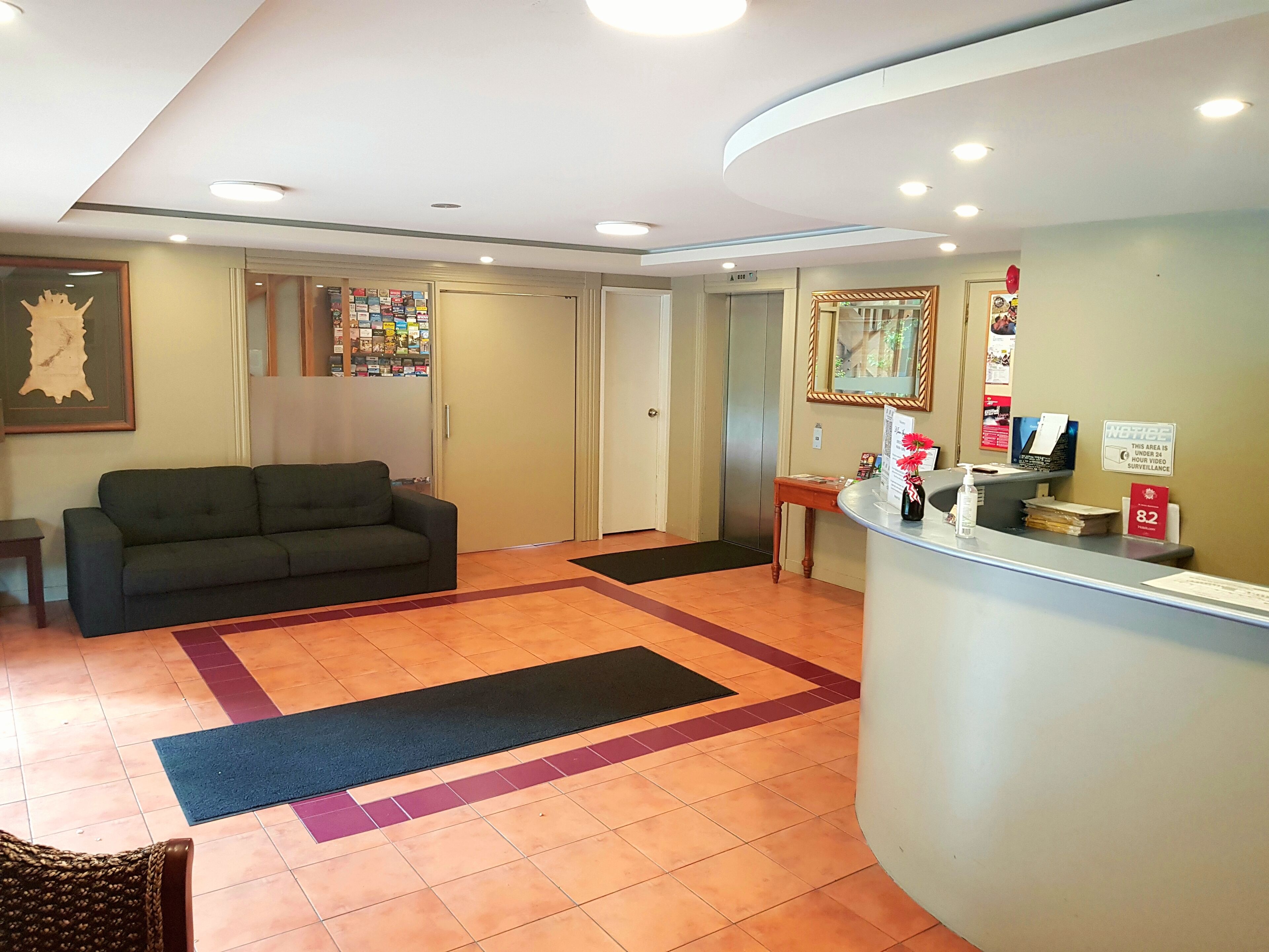 A reception area with a sofa, a reception desk, a framed picture on the wall, and a sign indicating surveillance.