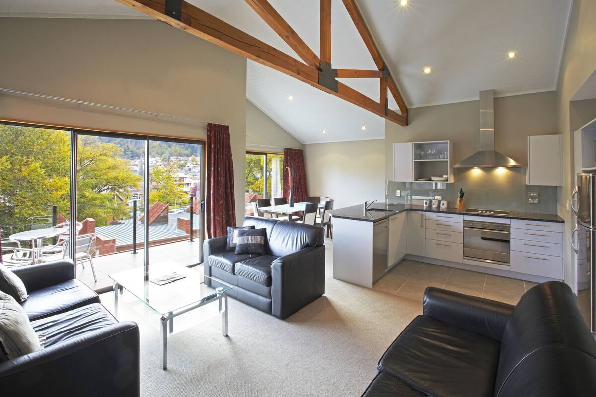 A modern kitchen with a central island, a dining area with a table and chairs, and a living area with a sofa and a glass coffee table.