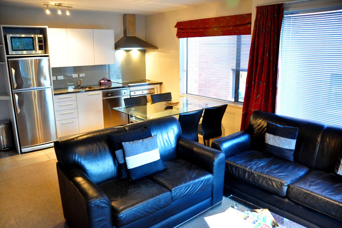 A compact living space with a kitchenette, a dining area, and a seating area with a black leather sofa.