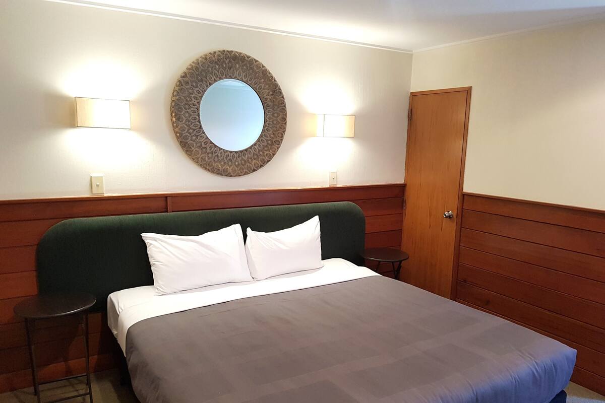 A hotel room with a bed, two bedside tables, a round mirror, and a door.
