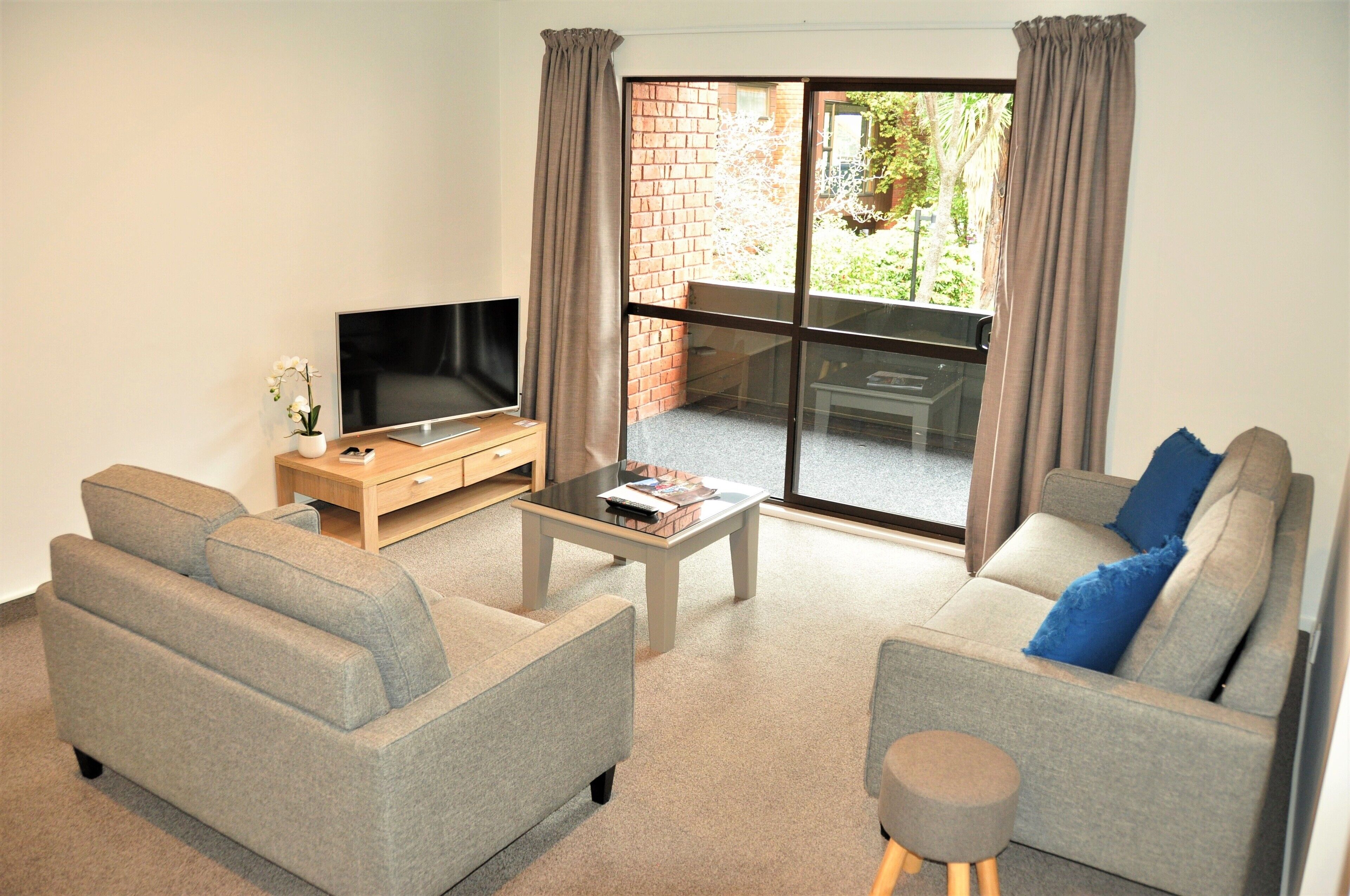 A modern living room with a grey sofa, a coffee table, a TV, and a sliding glass door to an outdoor area.