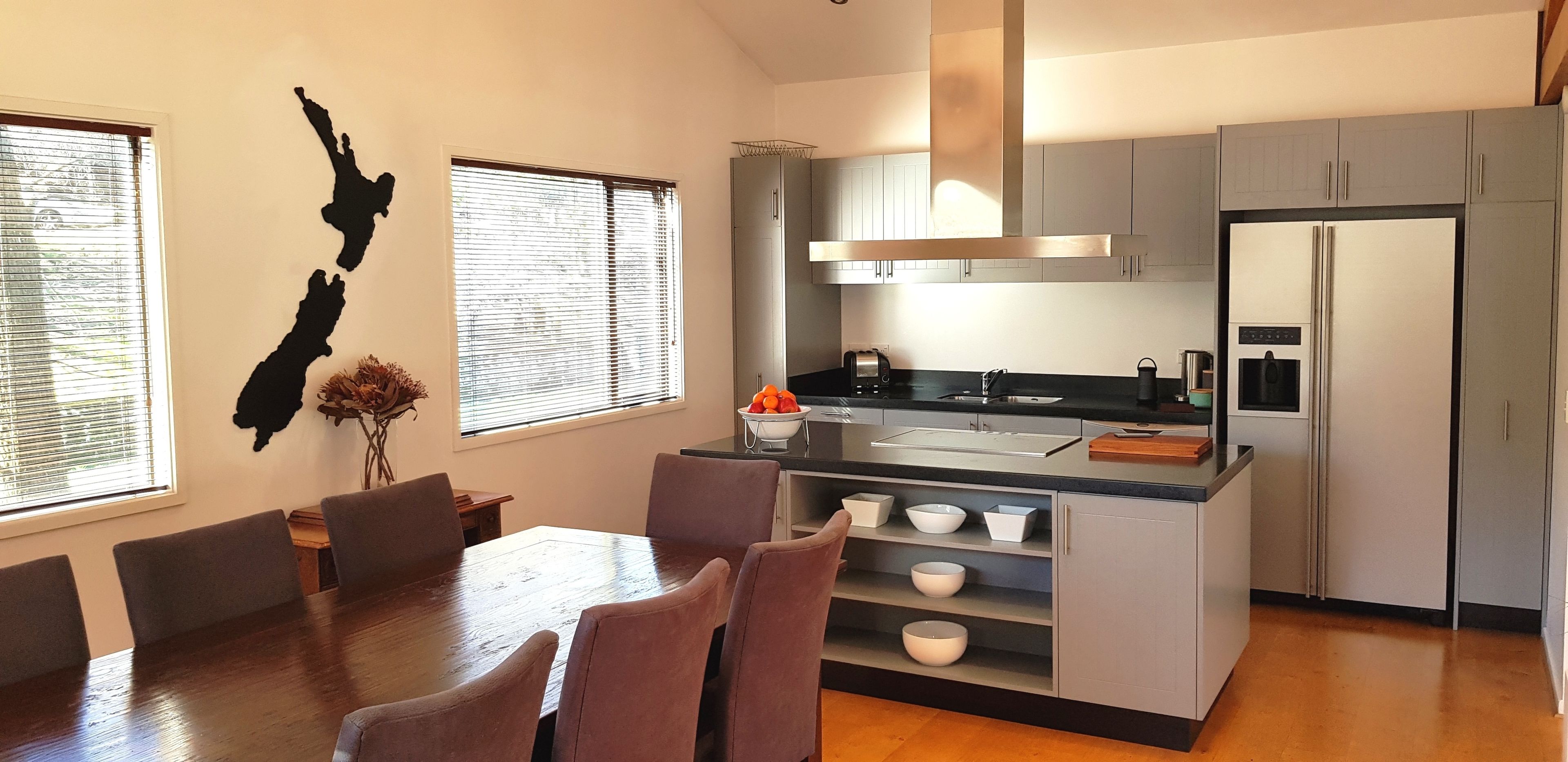 A modern kitchen with a central island, grey cabinets, and a dining area with a wooden table and chairs.