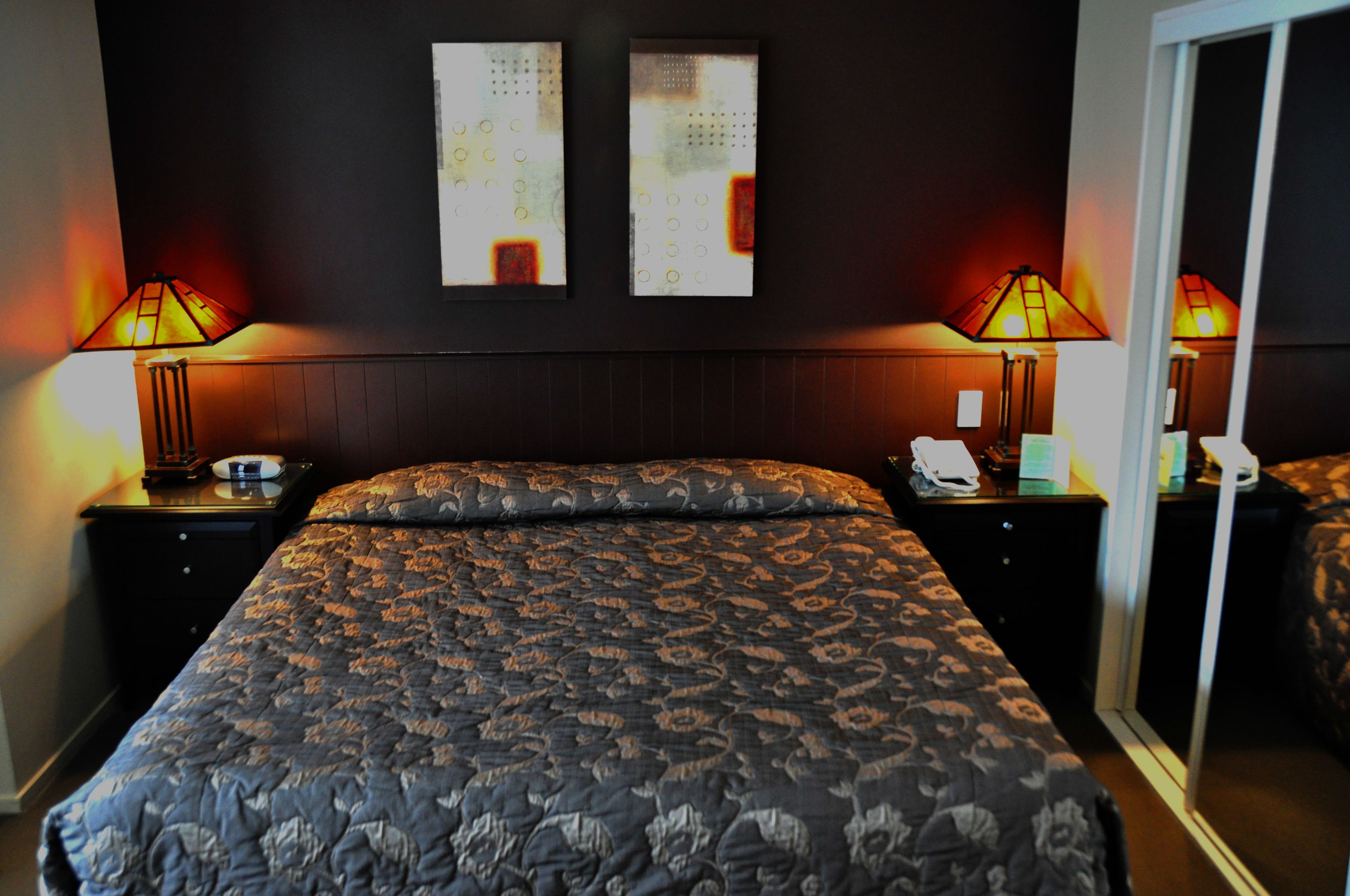 A hotel room with a large bed, two bedside tables, two wall-mounted lamps, and a sliding glass door.