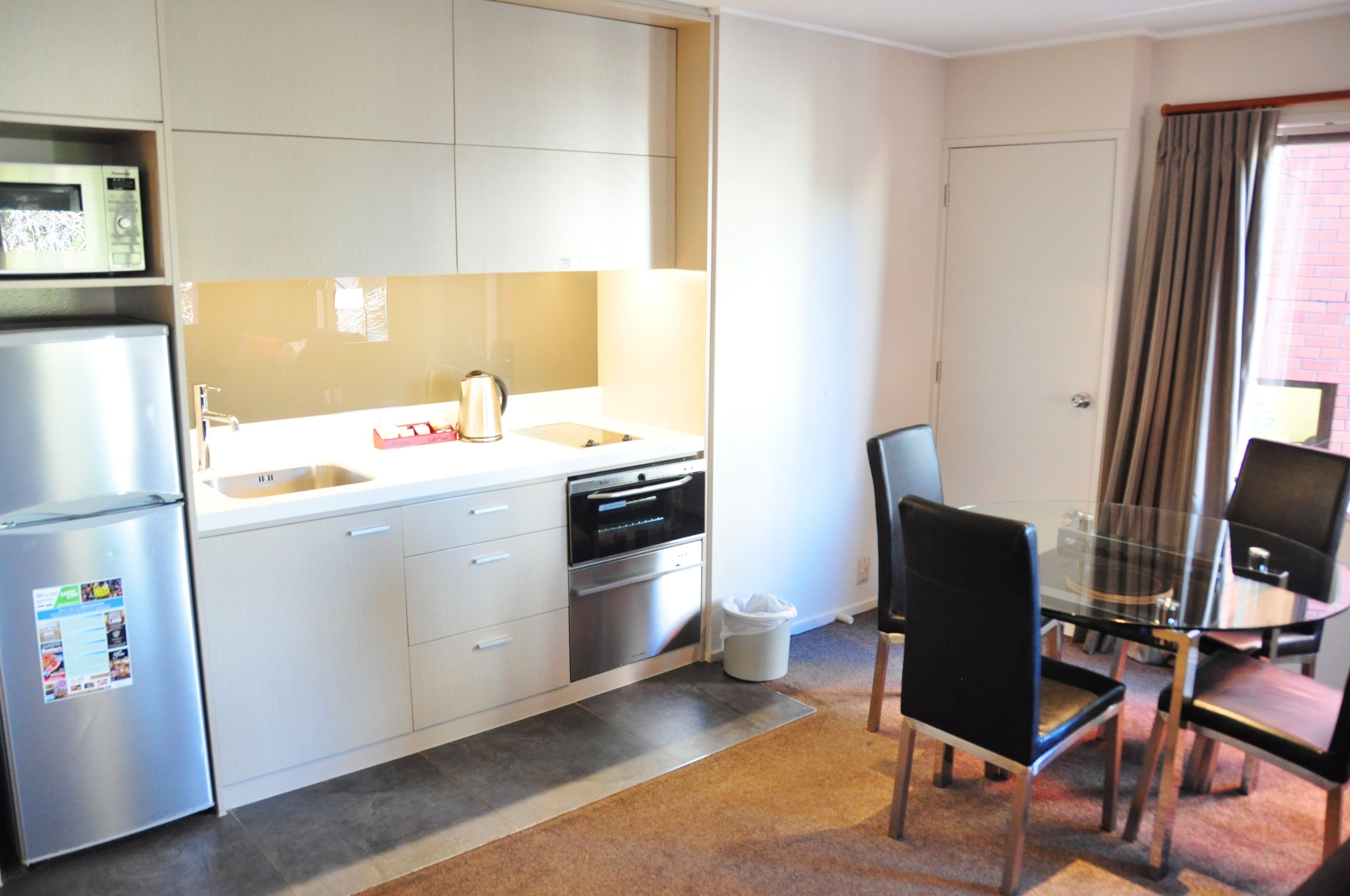 A compact kitchen with a refrigerator, oven, and sink. There is a dining table with chairs and a small television.