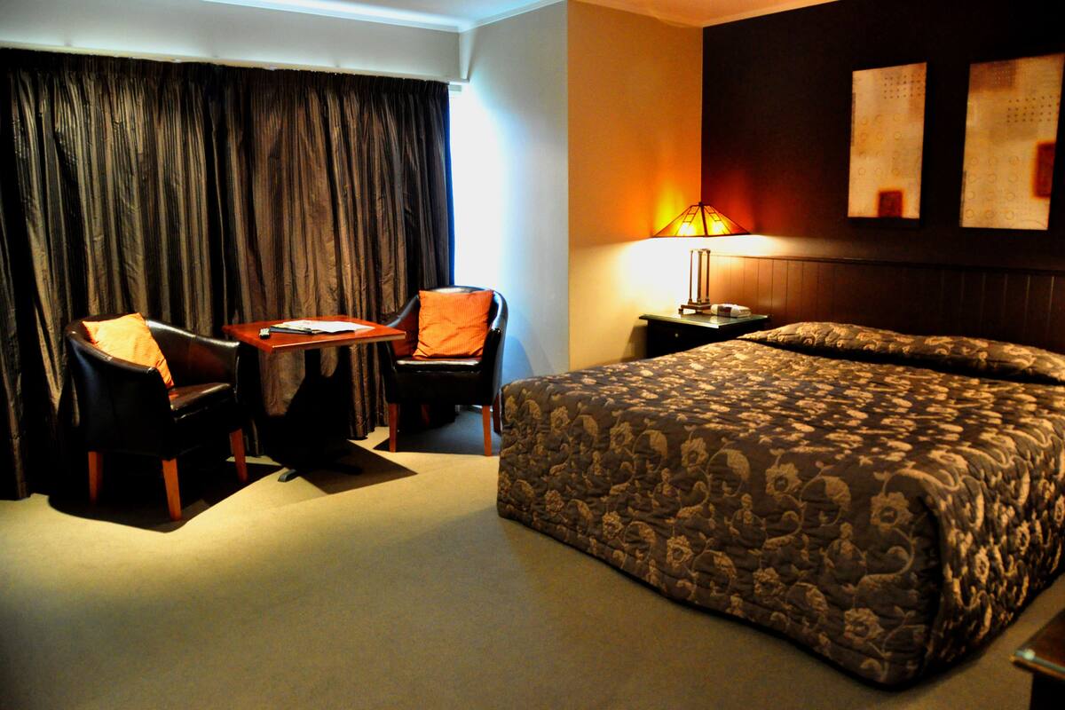 A hotel room with a large bed, a desk, a chair, and a lamp.