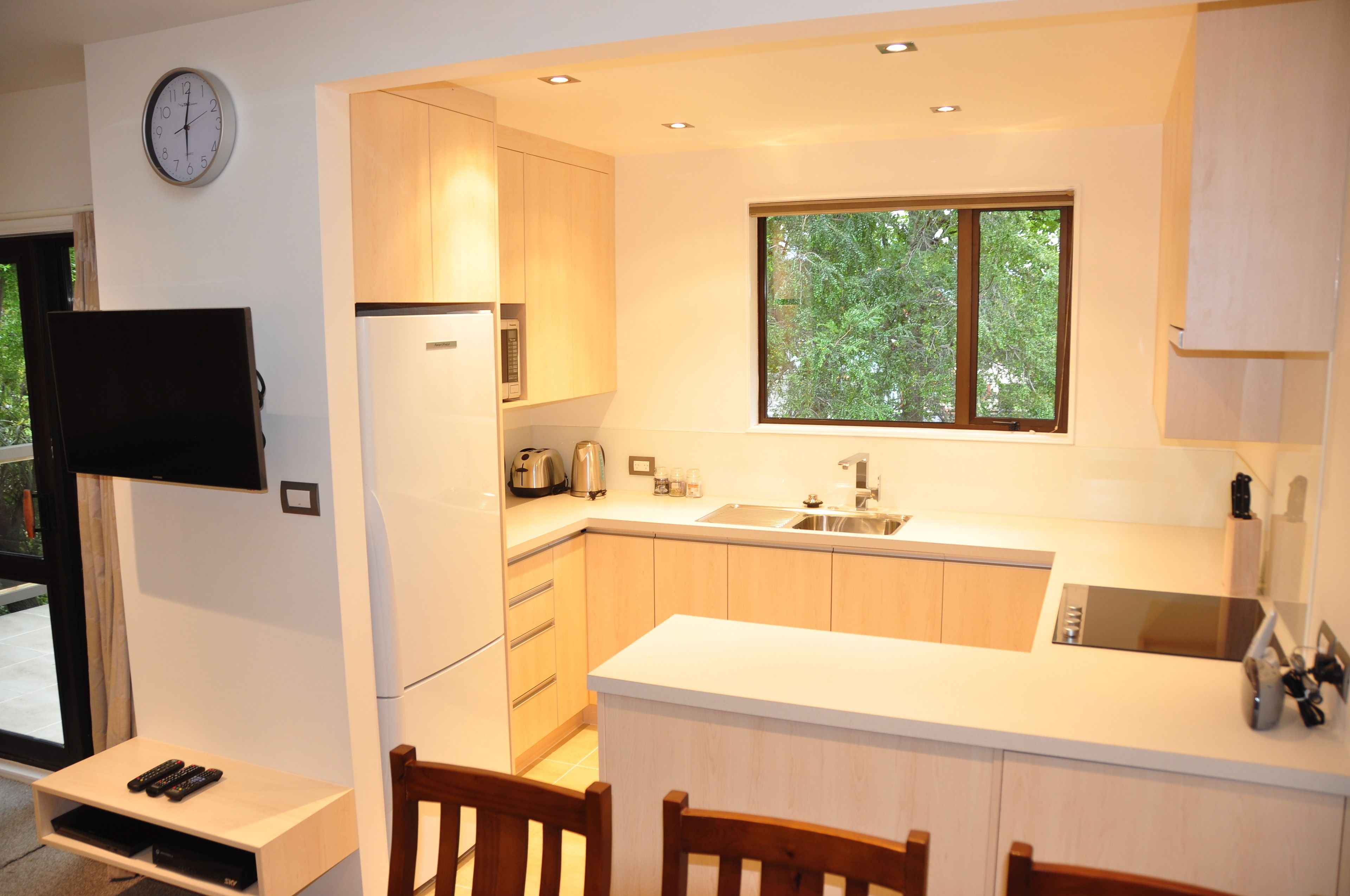 A modern kitchen with a built-in refrigerator, microwave, and sink. There is a window above the sink, and a clock on the wall.