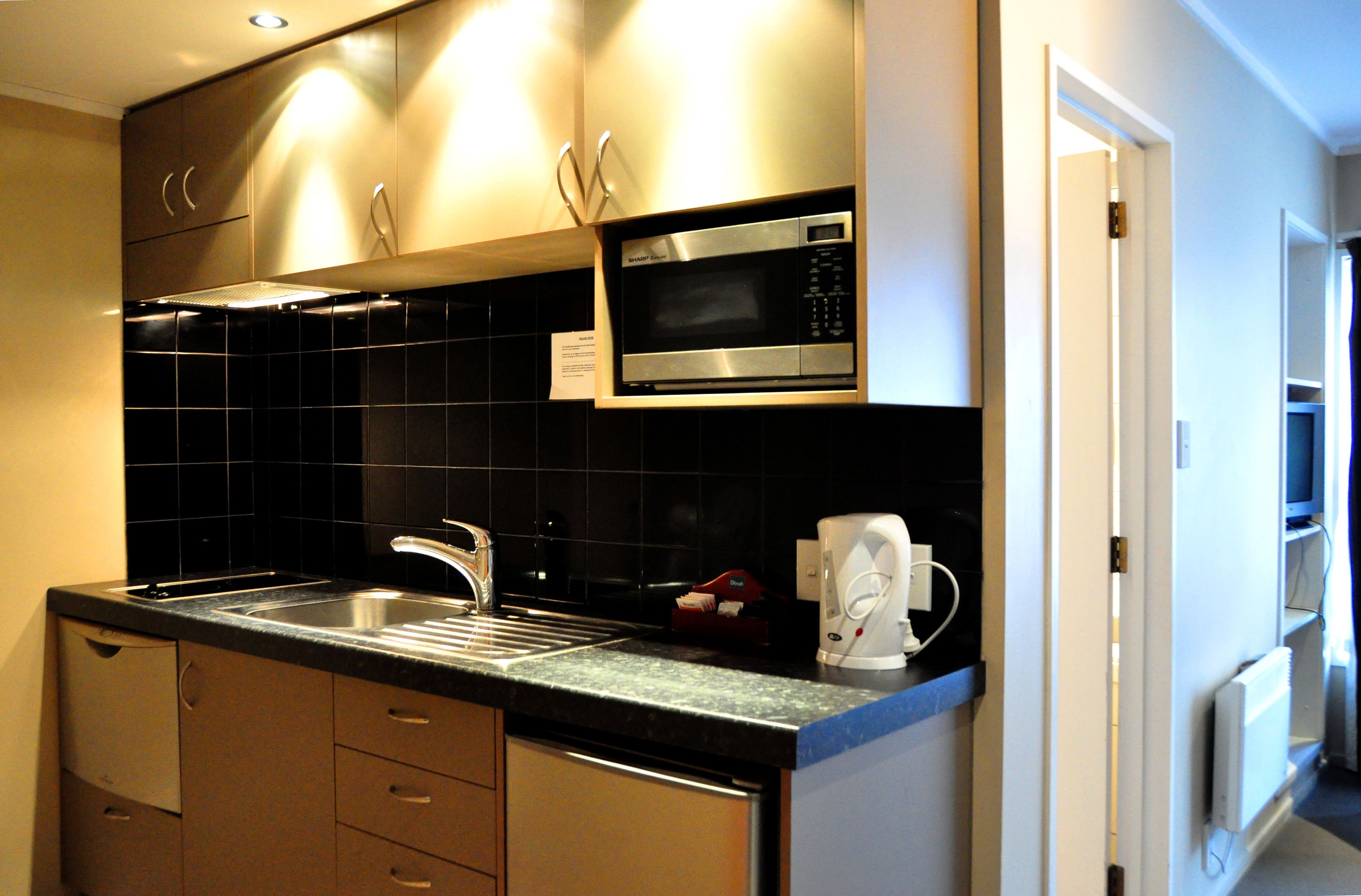 A modern kitchen with stainless steel appliances, a black tiled backsplash, and wooden cabinets.