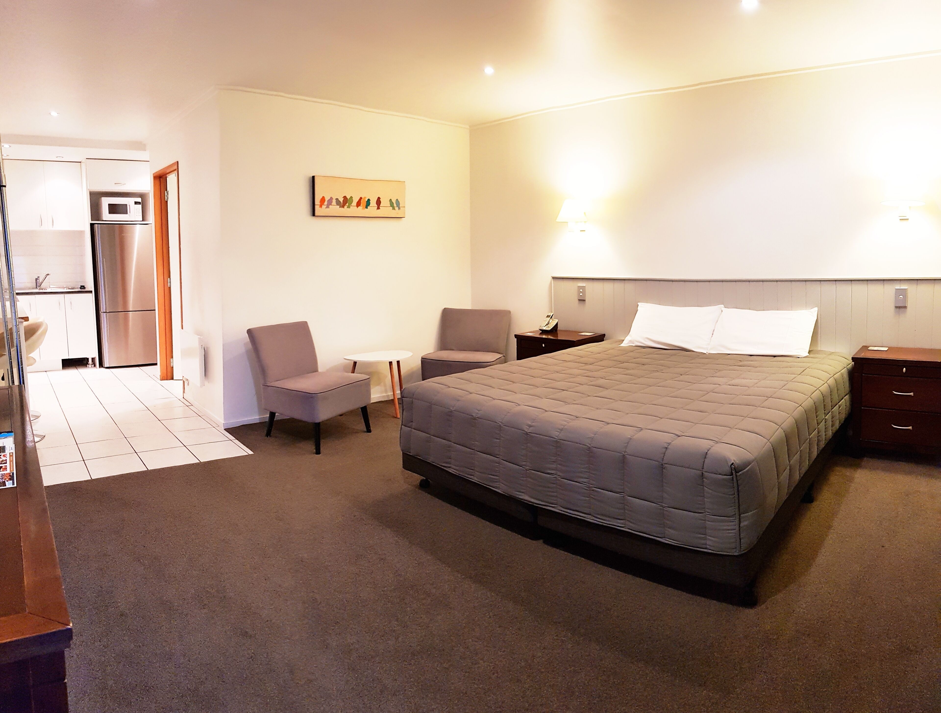 A hotel room with a large bed, two armchairs, a small table, a microwave, and a refrigerator.