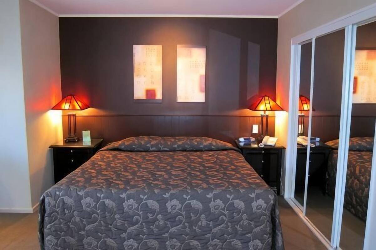 A hotel room with a bed, two bedside tables with lamps, a sliding glass door, and a dark-colored headboard.
