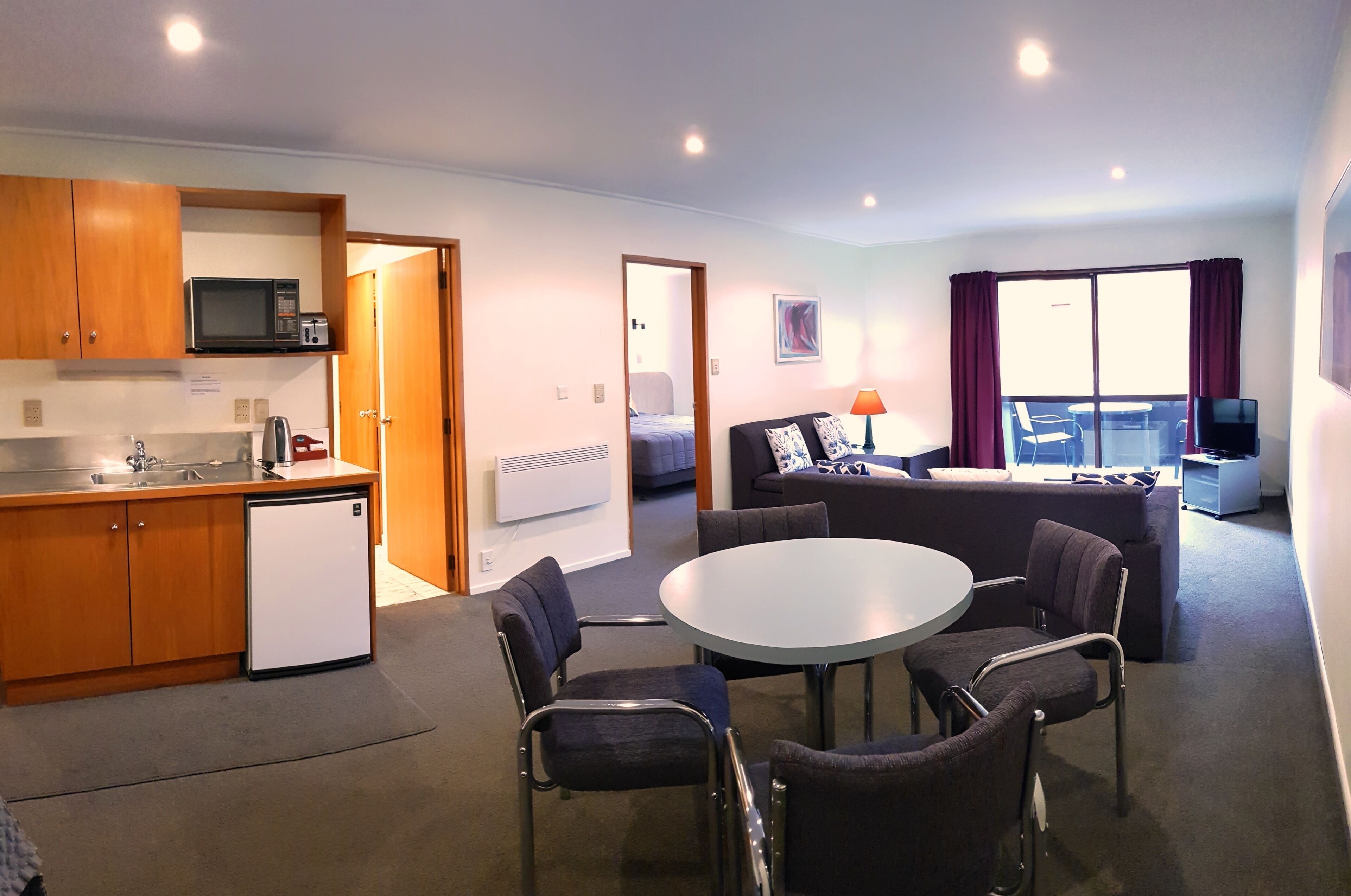A compact living space with a kitchenette, a dining area with a round table and chairs, a sofa, and a TV.