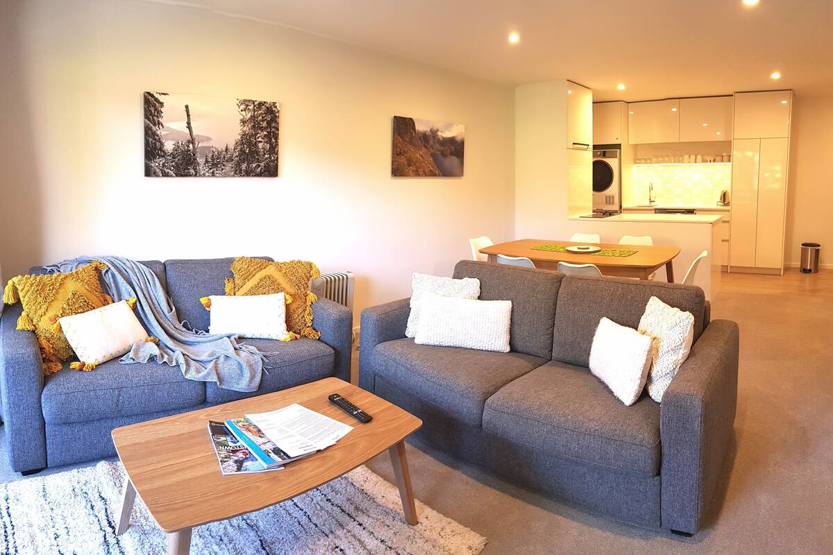 A modern living room with a grey sofa, a wooden coffee table, and a dining area with a table and chairs.