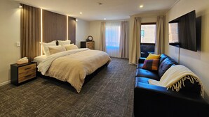 Una habitación de hotel moderna con una cama grande, un sofá, un televisor y un ventanal con cortinas.