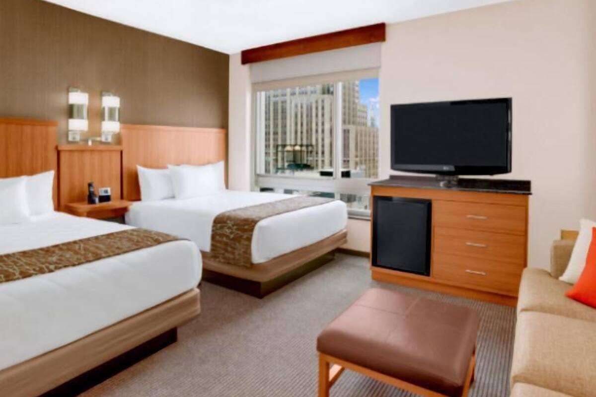 Ein Hotelzimmer mit zwei Betten, einem Fernseher, einem Schreibtisch und einem Fenster mit Blick auf die Stadt.