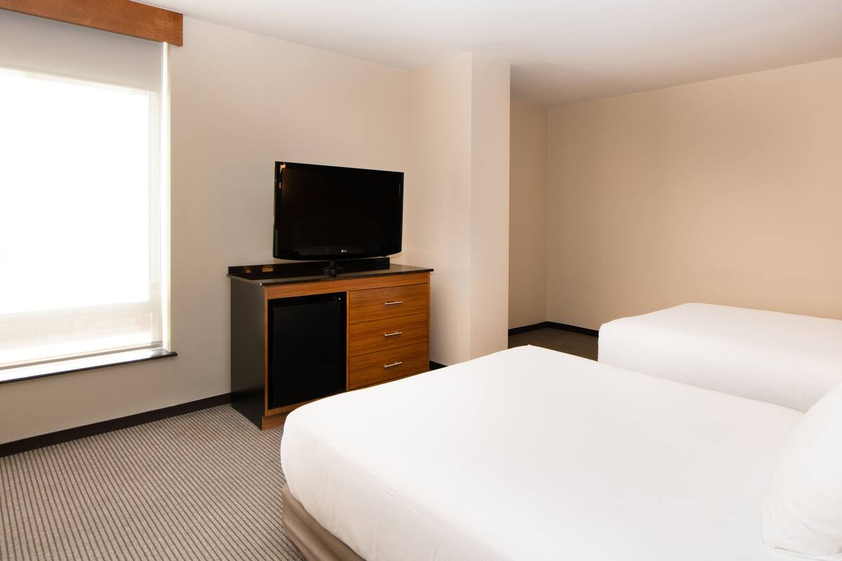 Ein Hotelzimmer mit Bett, Fernseher auf einem Holzschrank und einem Fenster.