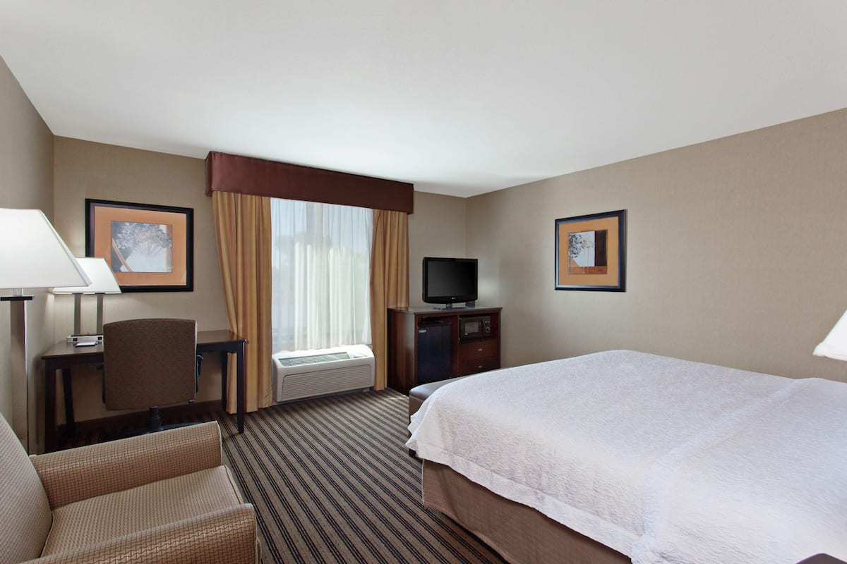 Quarto de hotel com cama, escrivaninha com cadeira, televisão e quadros nas paredes.