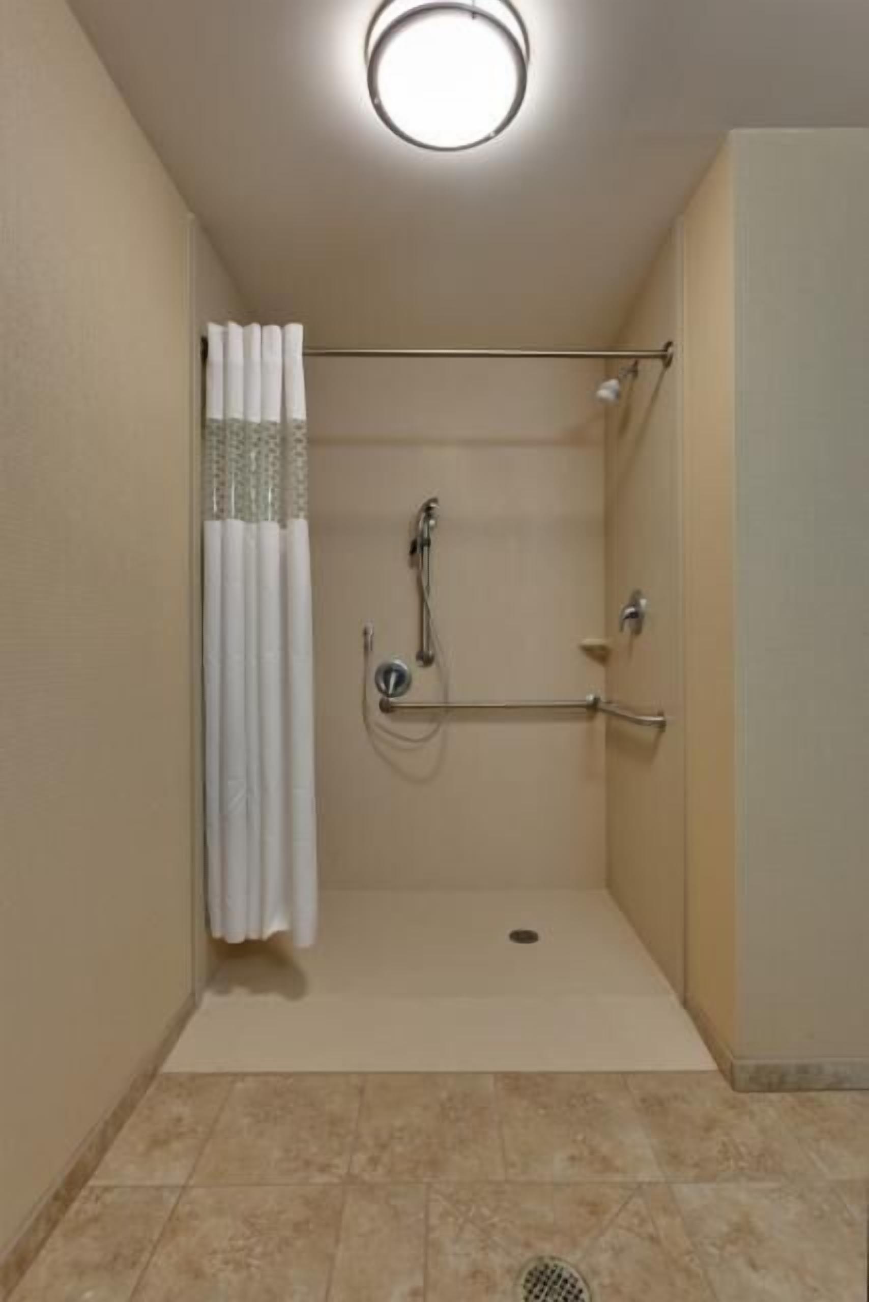 A small, enclosed shower area with a white curtain, a handheld showerhead, and a grab bar.