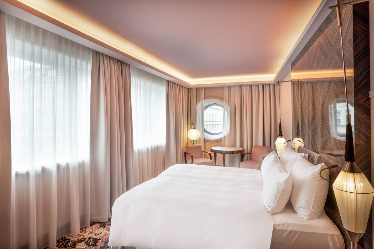 A hotel room with a large bed, a round table, a chair, and a lamp.