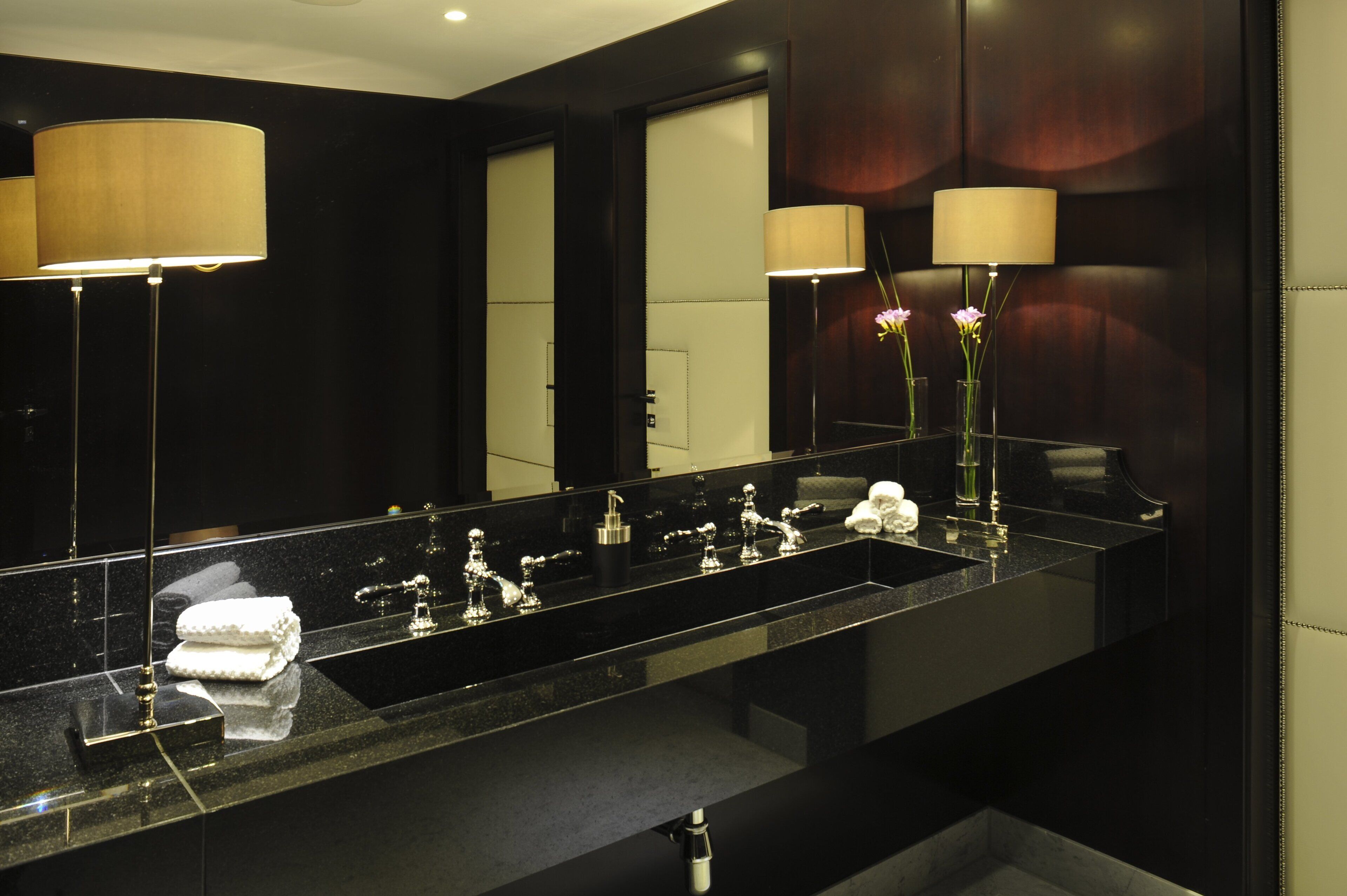 Un baño moderno con un espejo grande, encimera negra y dos lámparas de pared.