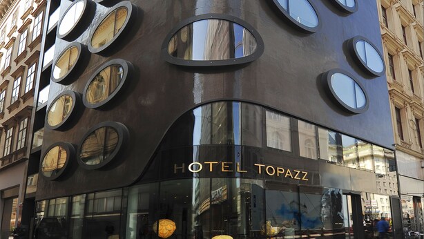 A modern building with a unique facade featuring circular windows and the name "HOTEL TOPAZZ" displayed prominently.