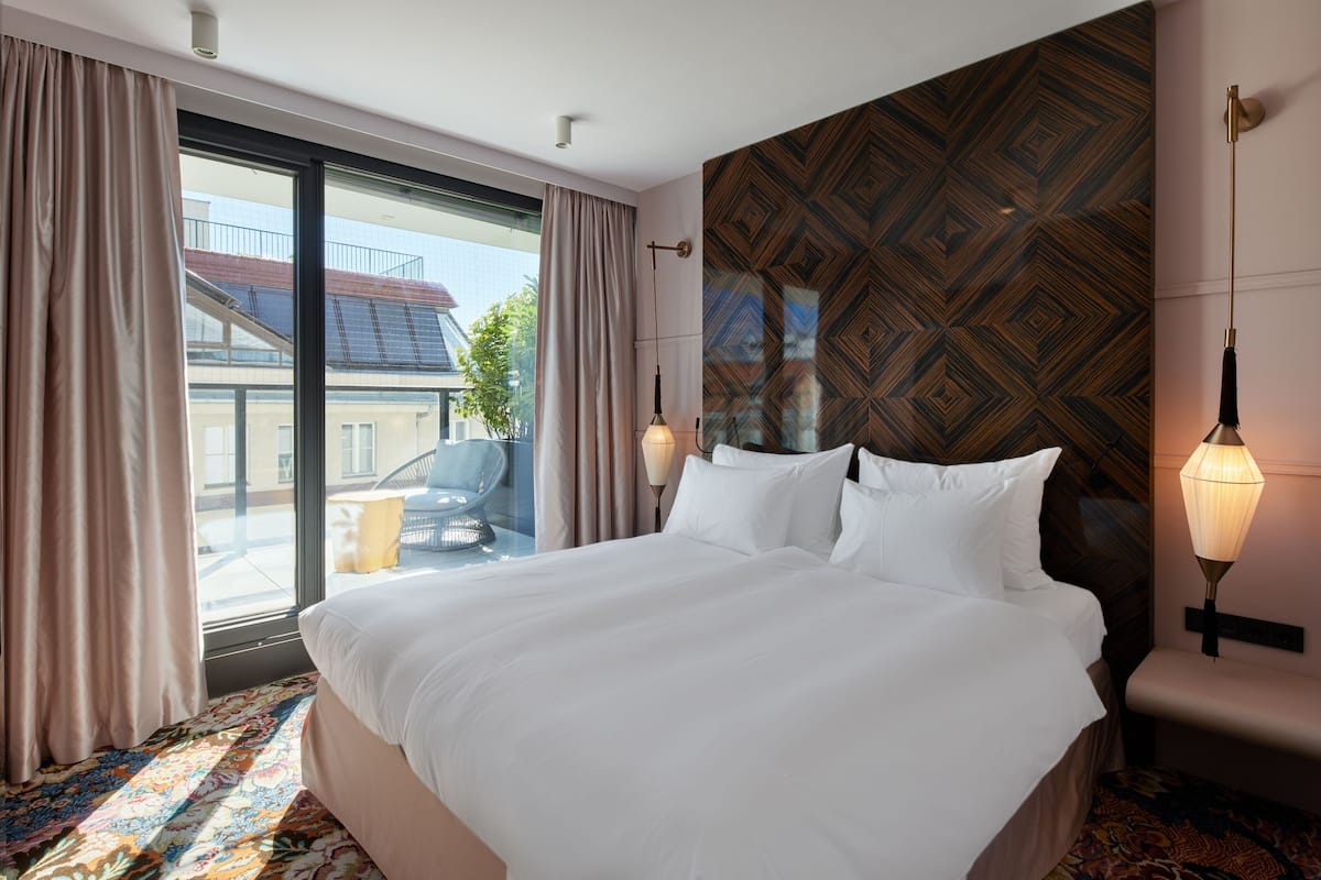 A hotel room with a large bed, a view of the outside, and a patterned wall.