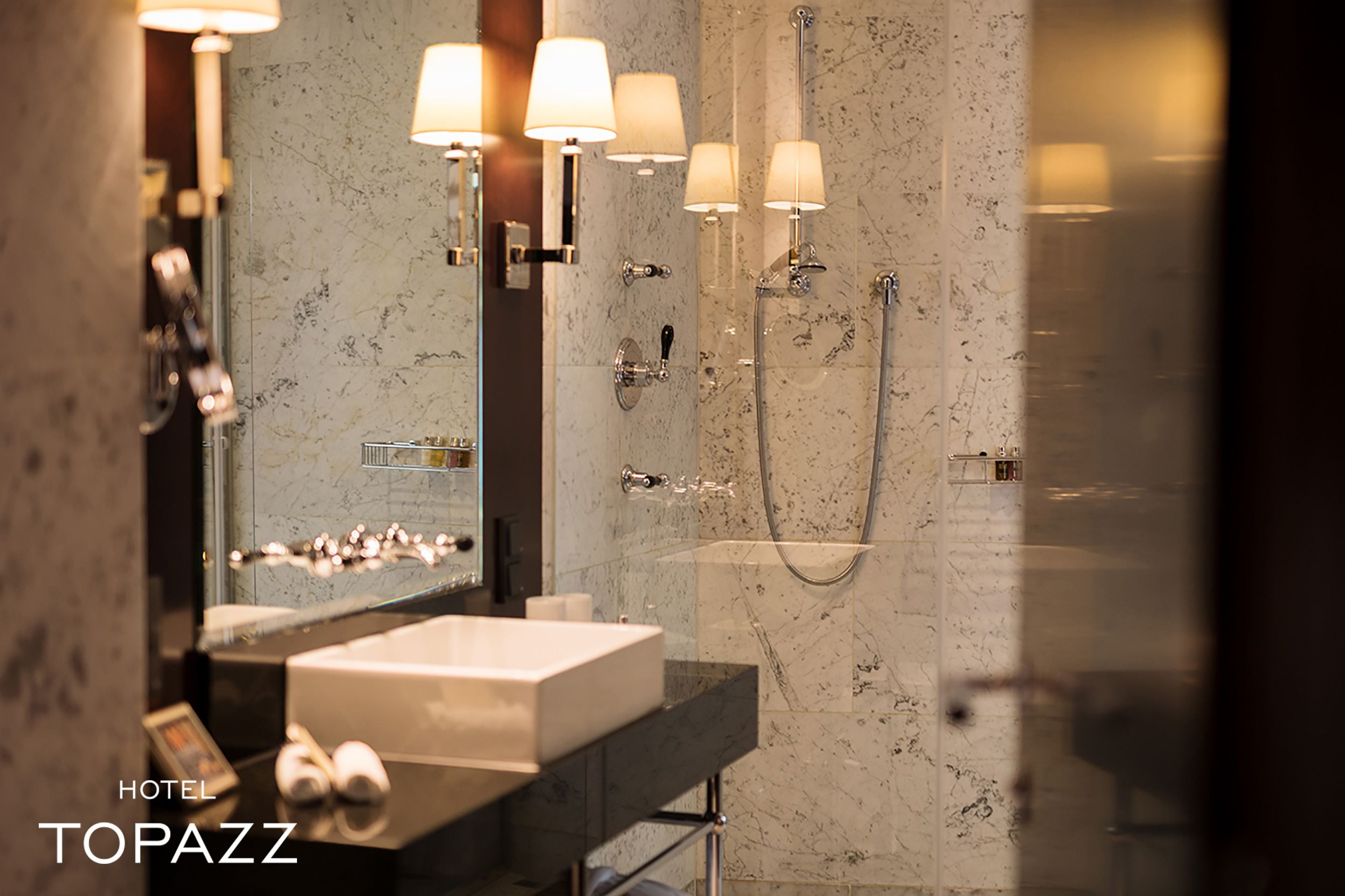 A modern bathroom with a marble sink, a large mirror, and a glass-enclosed shower.