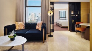 A hotel room with a black sofa, a round table, a bed, a desk, and a view of the city skyline.