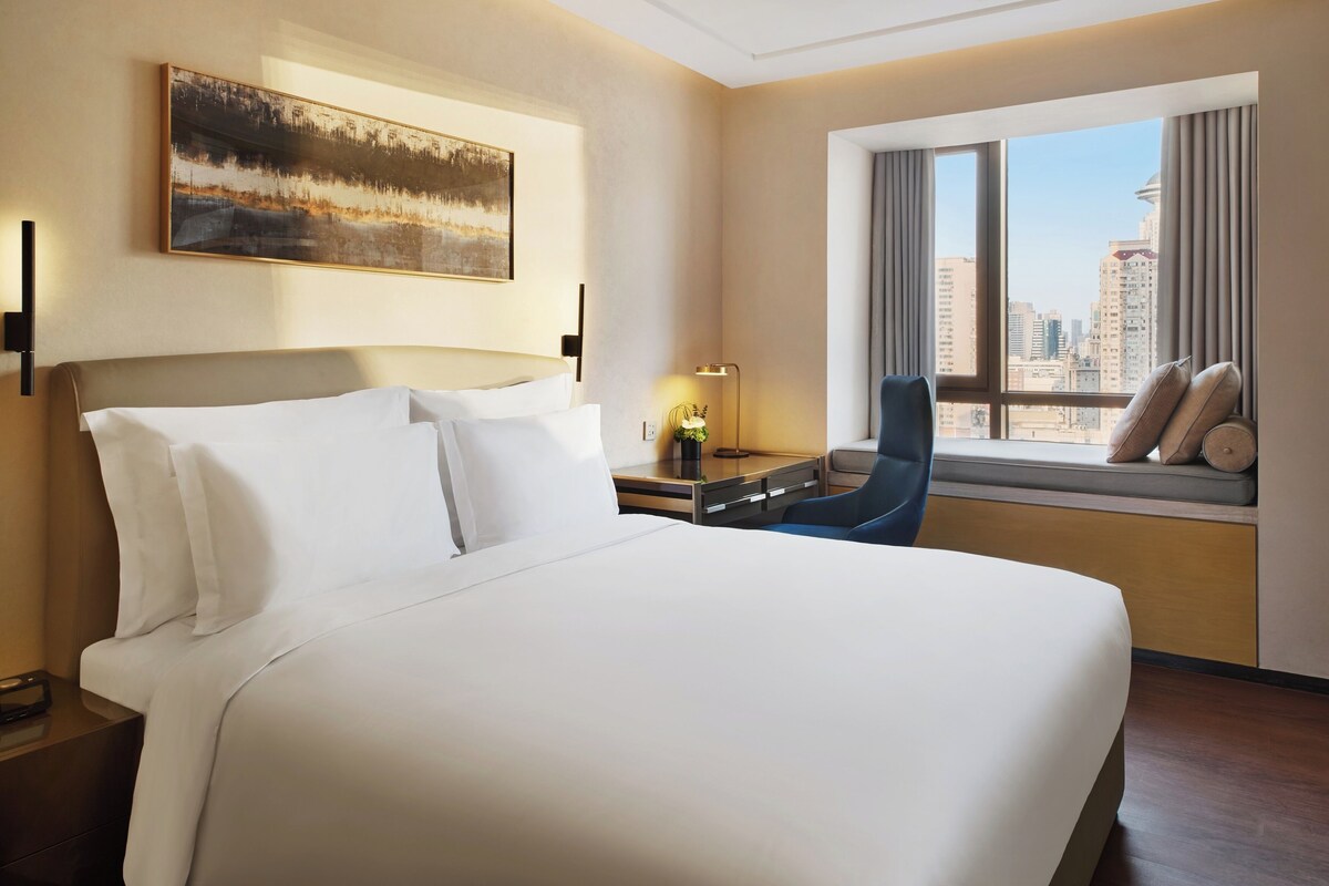Una habitación de hotel con una cama grande, un escritorio con una lámpara, una silla y una ventana con vista a la ciudad.