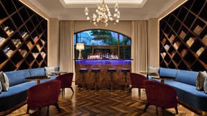 A bar area with a wooden bar counter, multiple stools, and a chandelier.