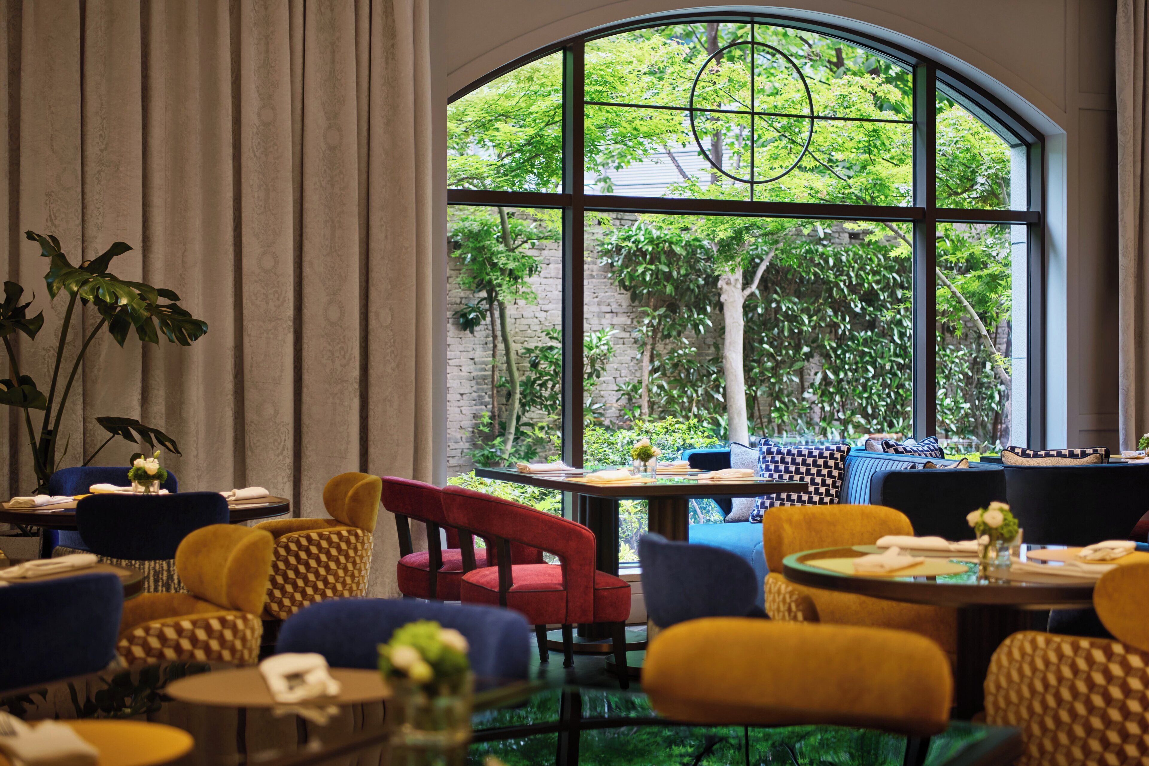 A restaurant with round tables, colorful chairs, and a large window with a view of greenery.