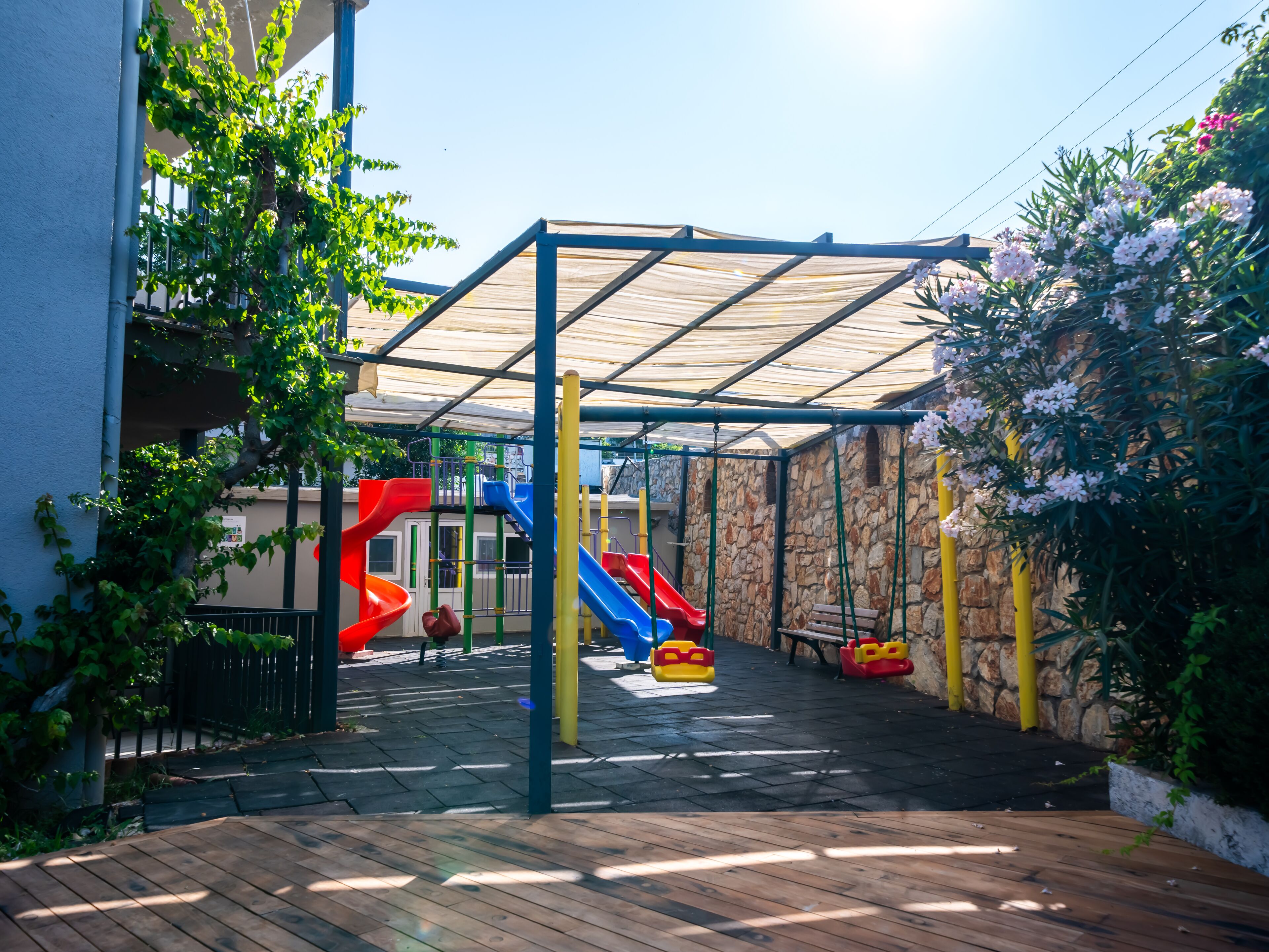 A covered outdoor play area with slides and climbing structures, surrounded by stone walls and greenery.