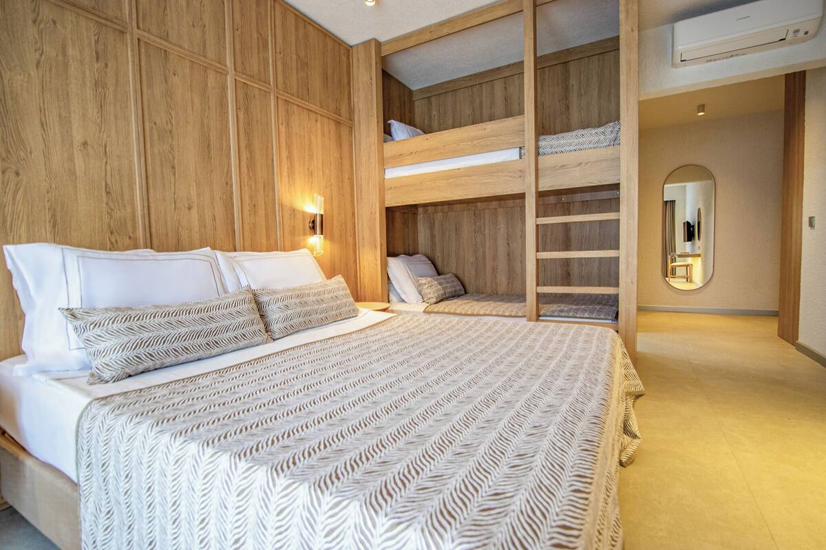 A bedroom with a large bed, a bunk bed, wooden paneling, a mirror, and a wall-mounted light fixture.