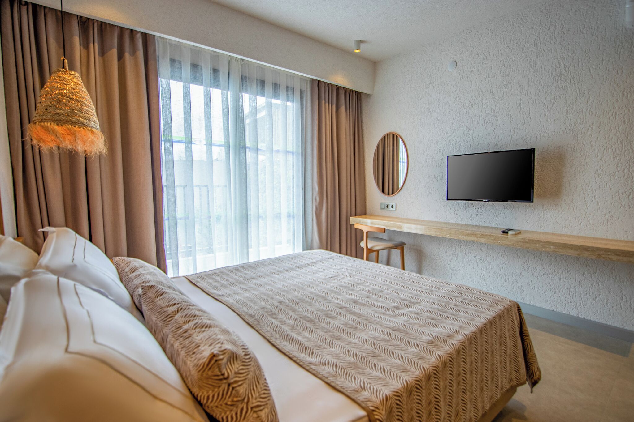 Habitación de hotel con una cama grande, un escritorio con televisor y vistas al exterior a través de amplios ventanales.