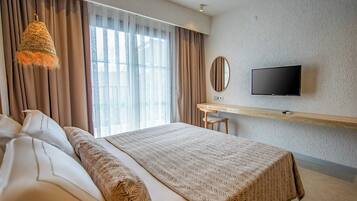 Habitación de hotel con una cama grande, un escritorio con televisor y vistas al exterior a través de amplios ventanales.