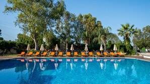 A swimming pool with orange lounge chairs and umbrellas, surrounded by trees and greenery. - Bodrum Beach Resort (Bodrum)
