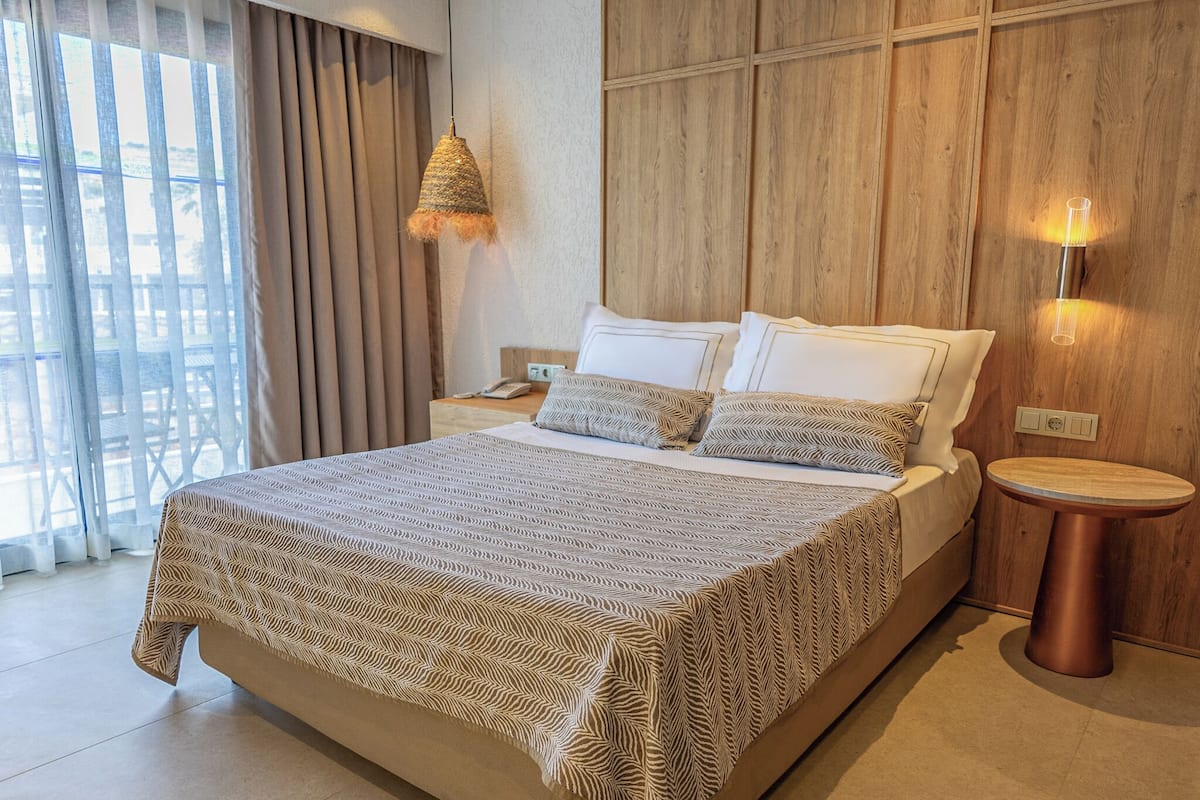 A modern hotel room with a large bed, wooden panel walls, and a view of the outdoors.
