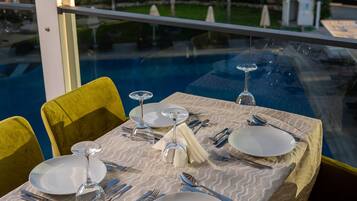 A dining table set for four with a view of a swimming pool and greenery.