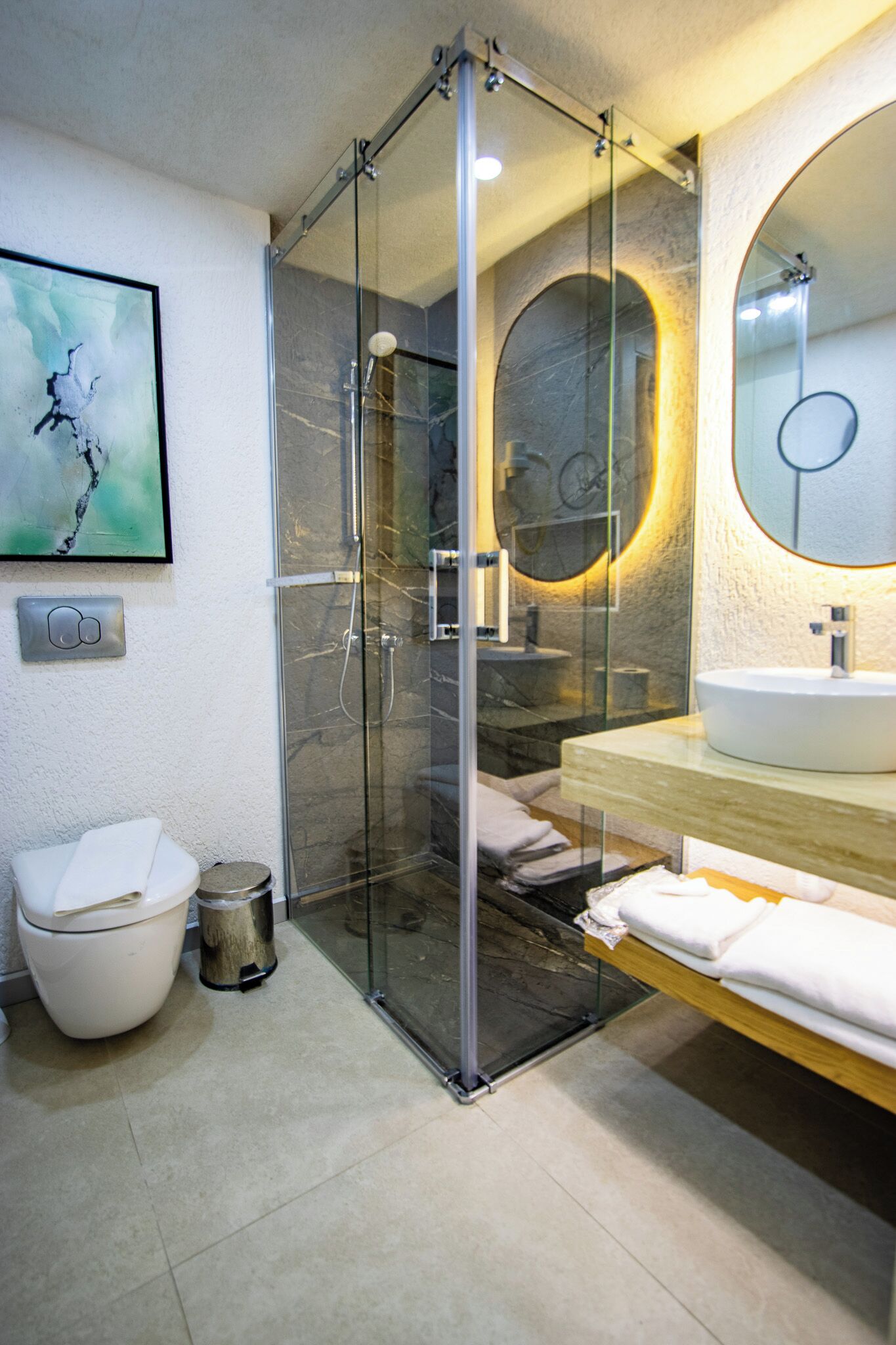 A modern bathroom with a glass-enclosed shower, a white toilet, a sink with a mirror, and a framed artwork on the wall.