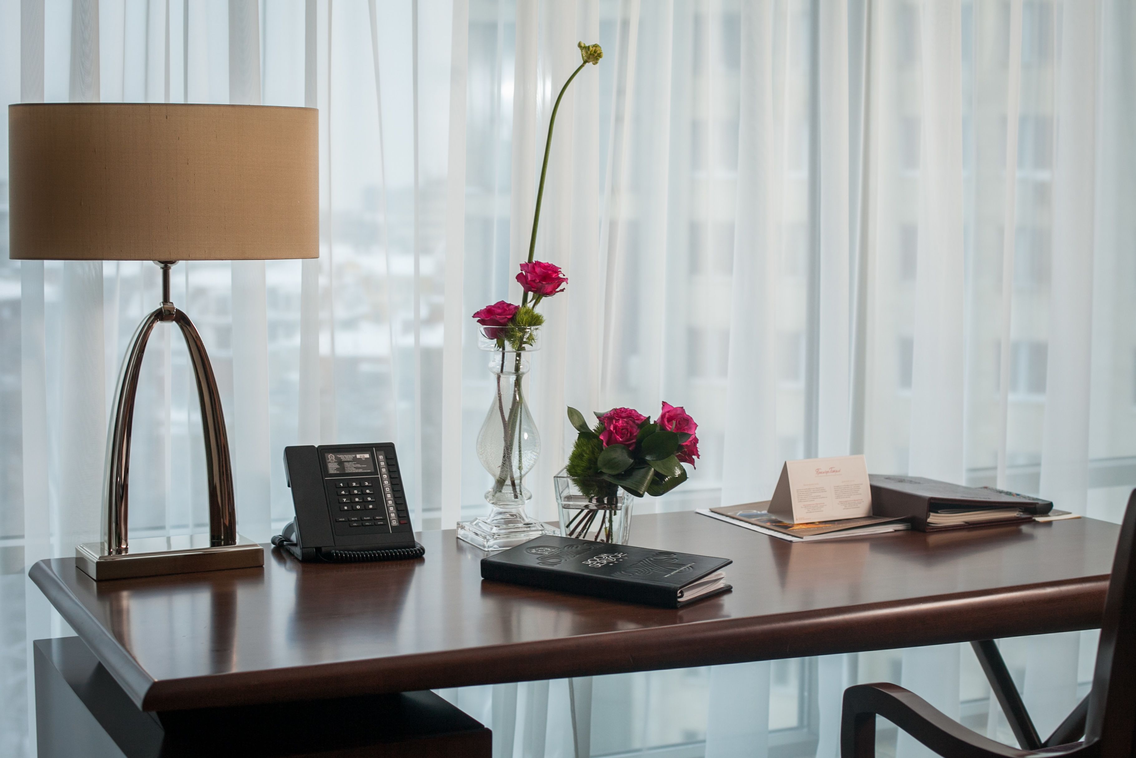 Un escritorio de madera con un teléfono, un florero con flores y un libro.