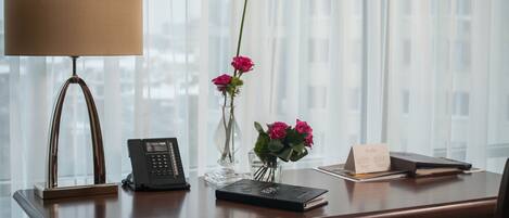 Un escritorio de madera con un teléfono, un florero con flores y un libro.