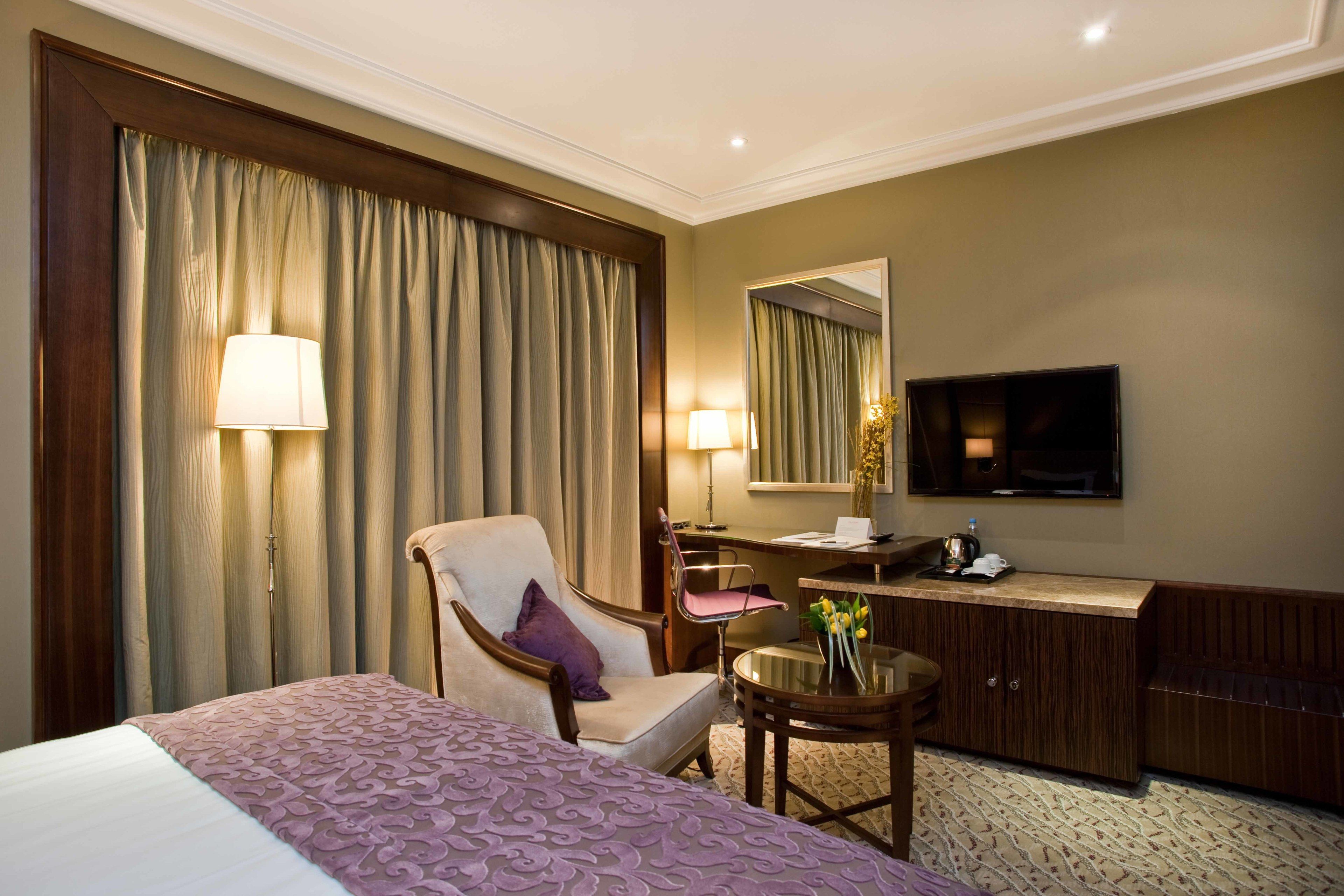 Una habitación de hotel con una cama, un escritorio, una silla, un televisor y un espejo.