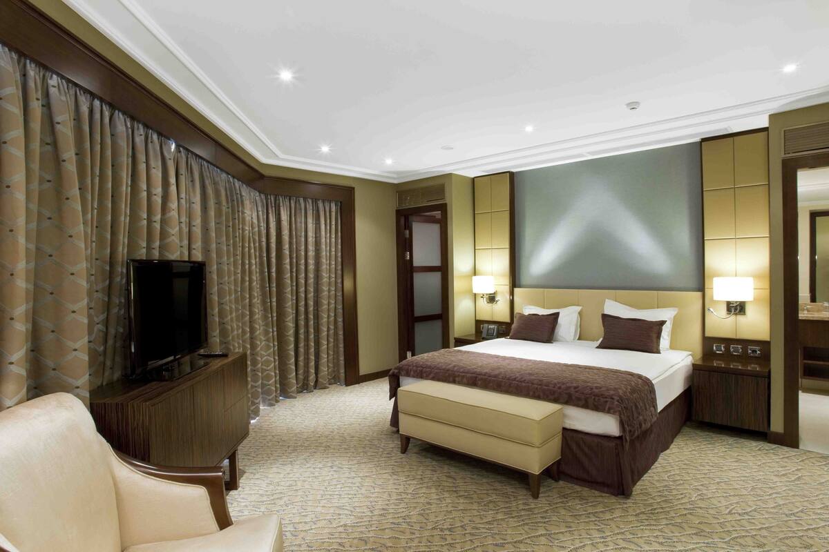 A hotel room with a large bed, a television on a wooden cabinet, a bedside table with a lamp, and a mirror on the wall.