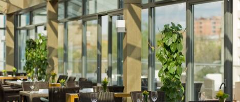 Un restaurante con terraza, amplias ventanas y plantas en macetas.