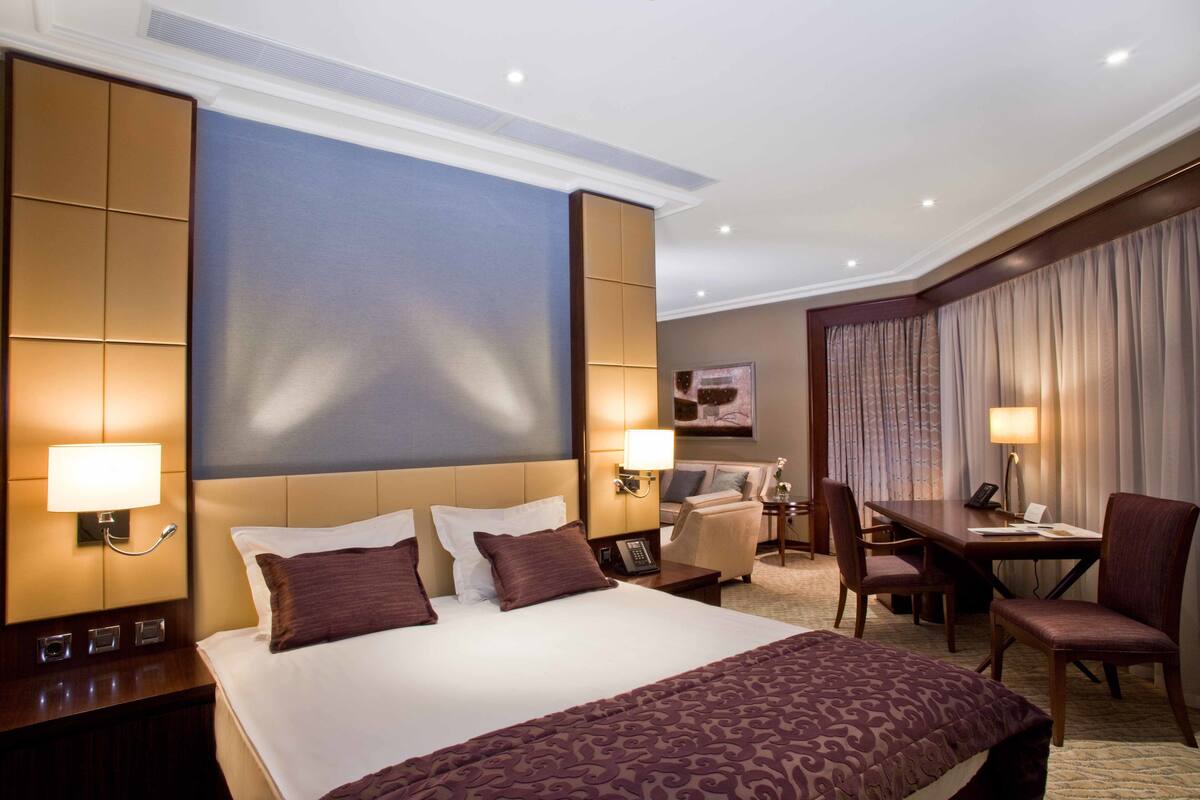 A hotel room with a large bed, a desk, a chair, and a television.